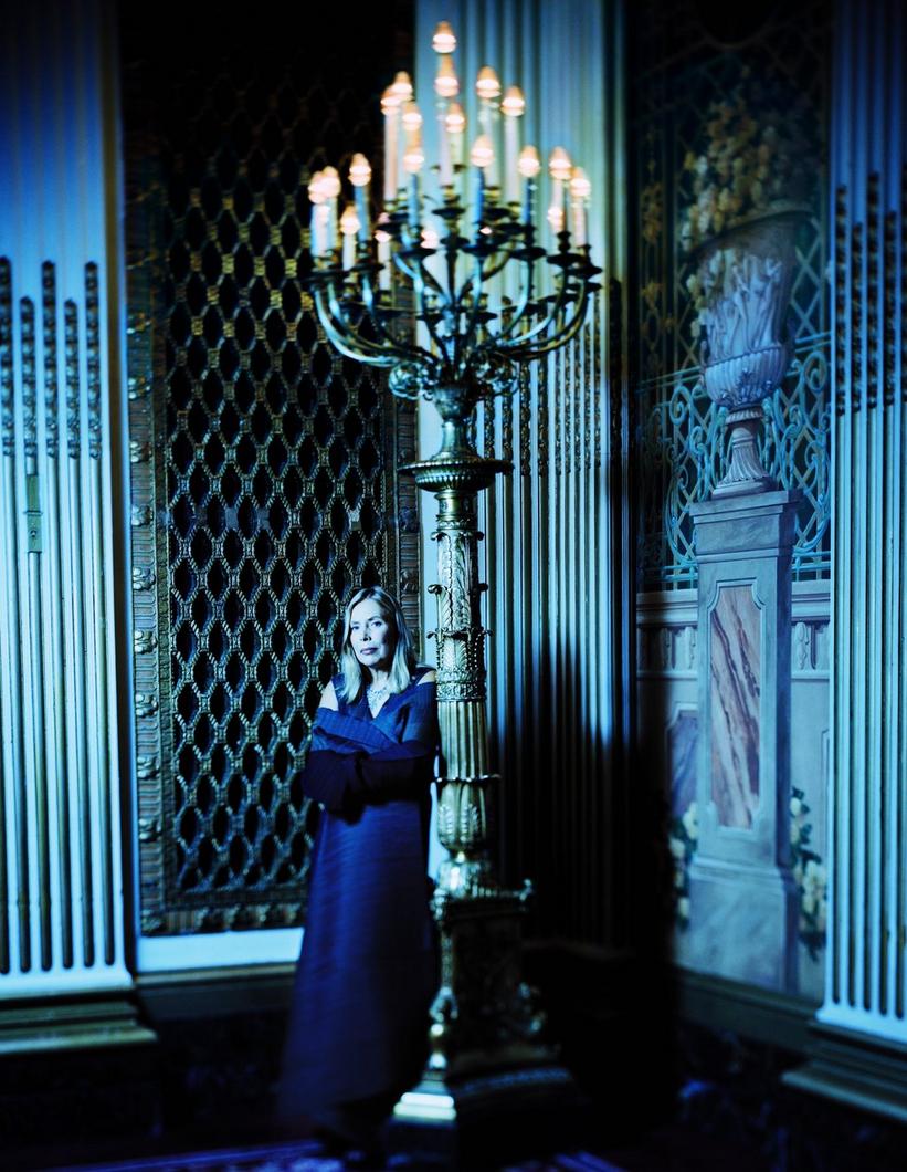 Joni Mitchell stands in a room next to a large candelabra in a film photo with a blue hue